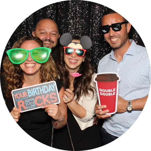 Four people posing with props in a photo booth; holding props with celebratory messages.