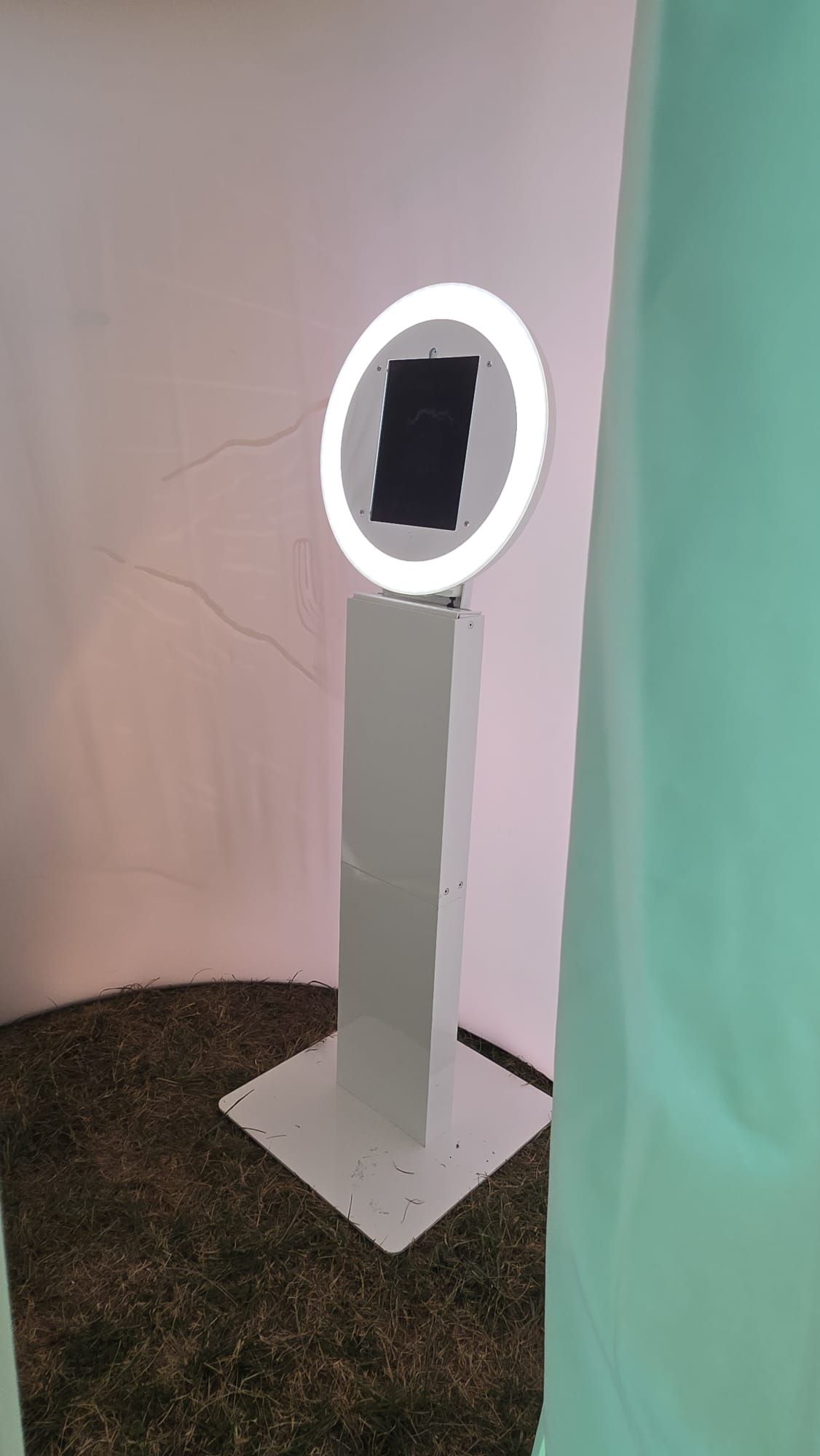 White photo booth with a glowing ring light, set against pink and green fabric.