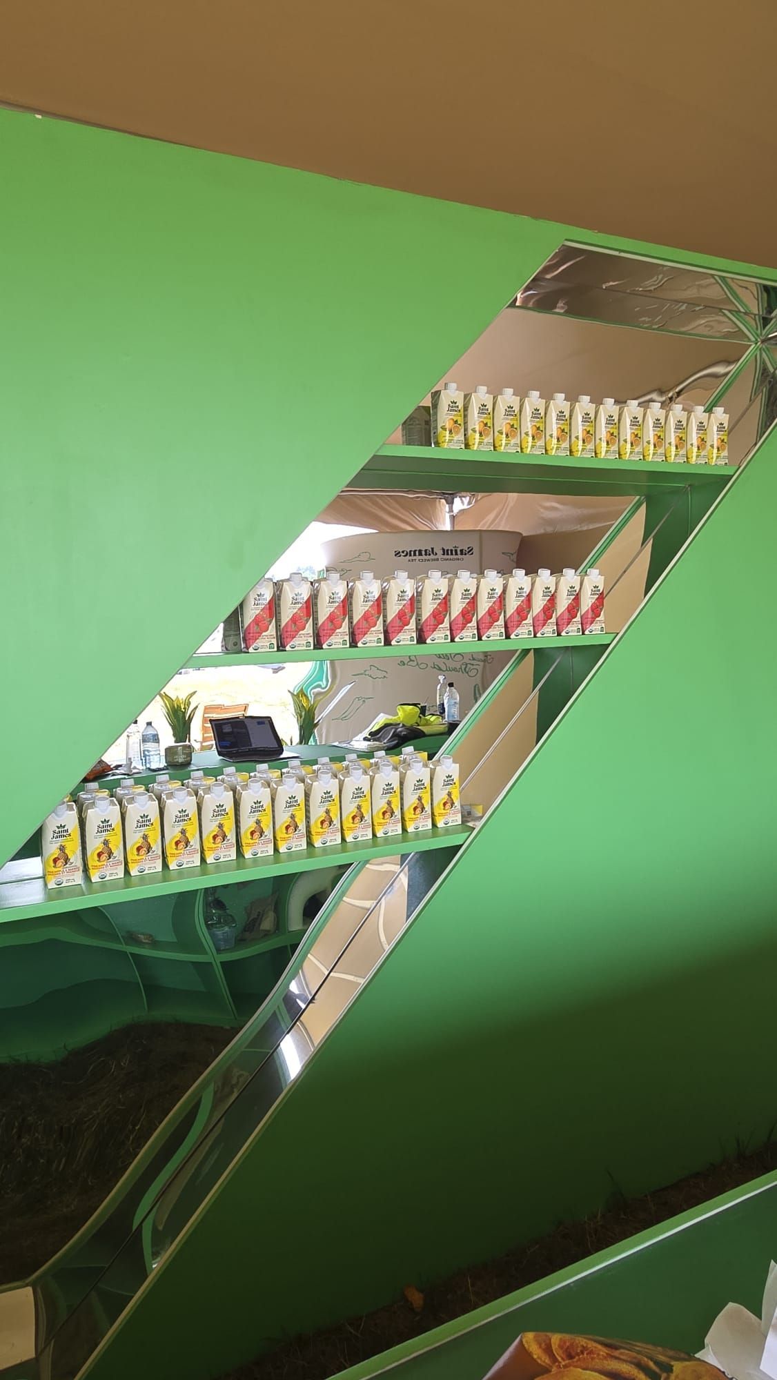 Green angled shelving unit holding rows of packaged products; mostly juice boxes, in a store.
