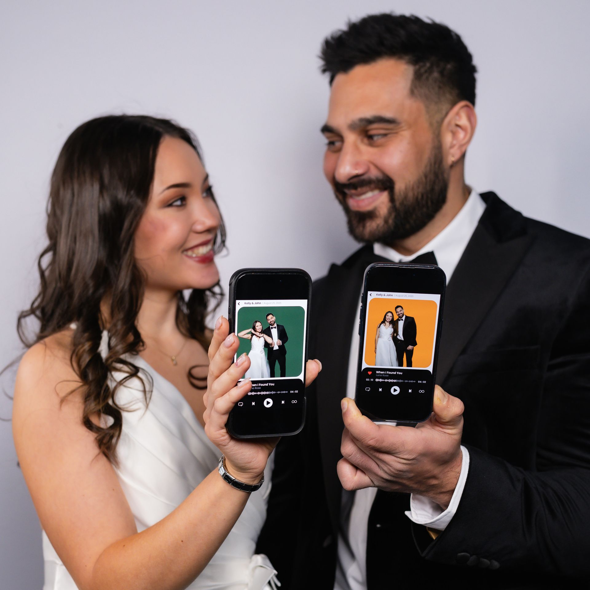 A smiling couple holds smartphones, each displaying a photo of a bride and groom against a colored backdrop.