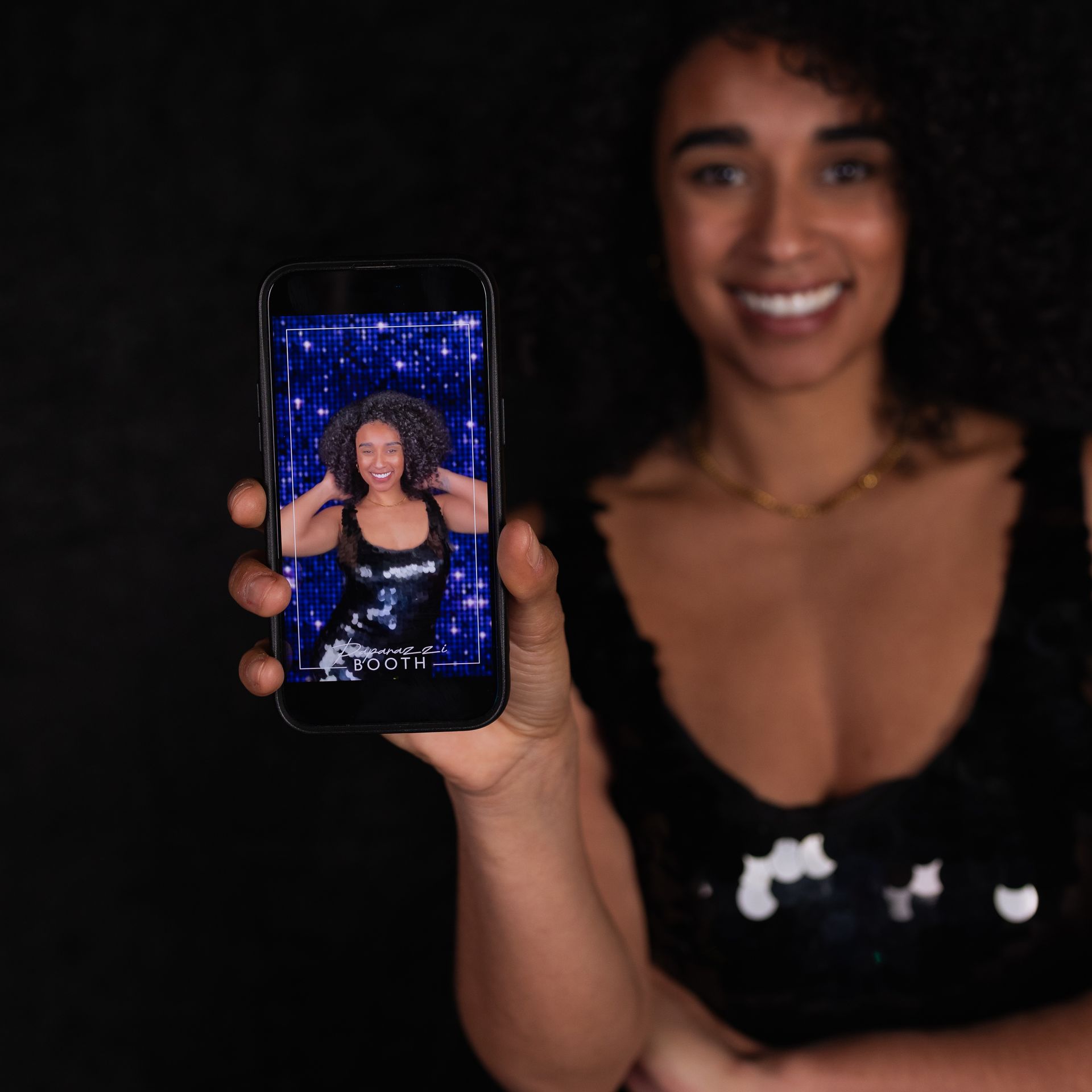 Woman smiling, holding phone displaying photo of herself with a starry background; black dress.