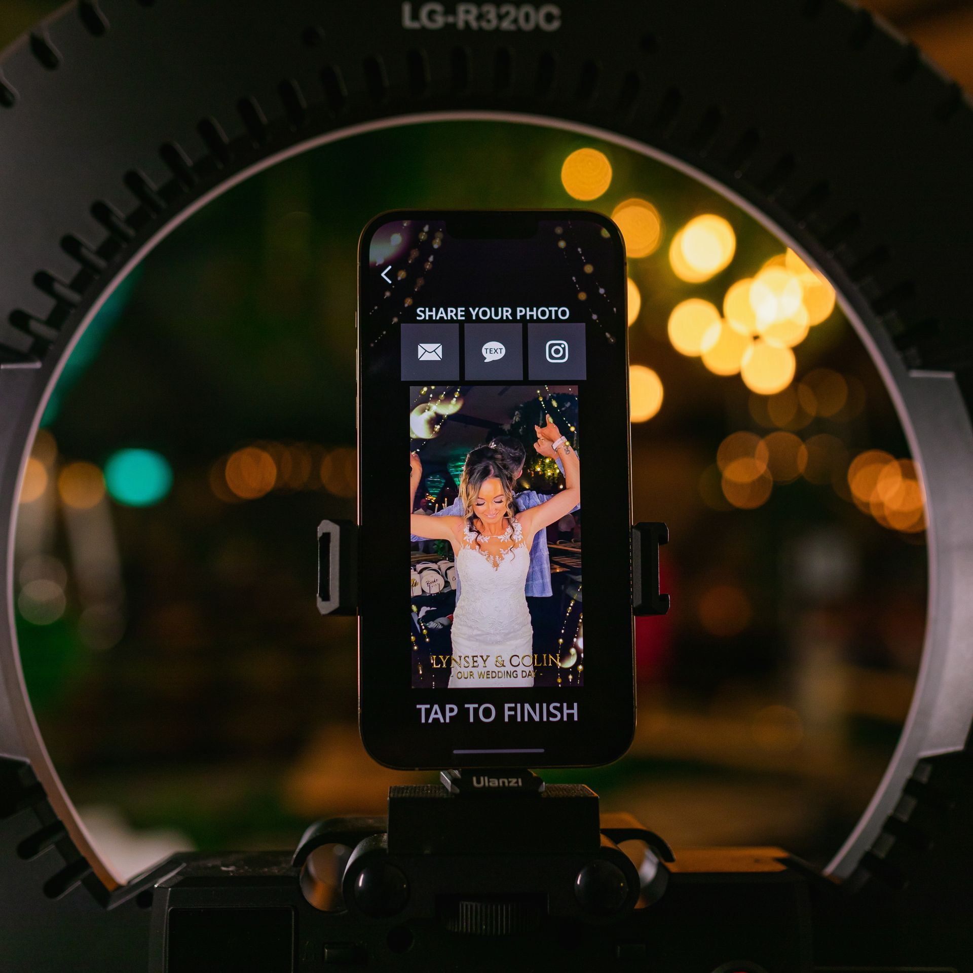 Smartphone displaying a photo, held in a ring light at an event, with blurred lights in the background.