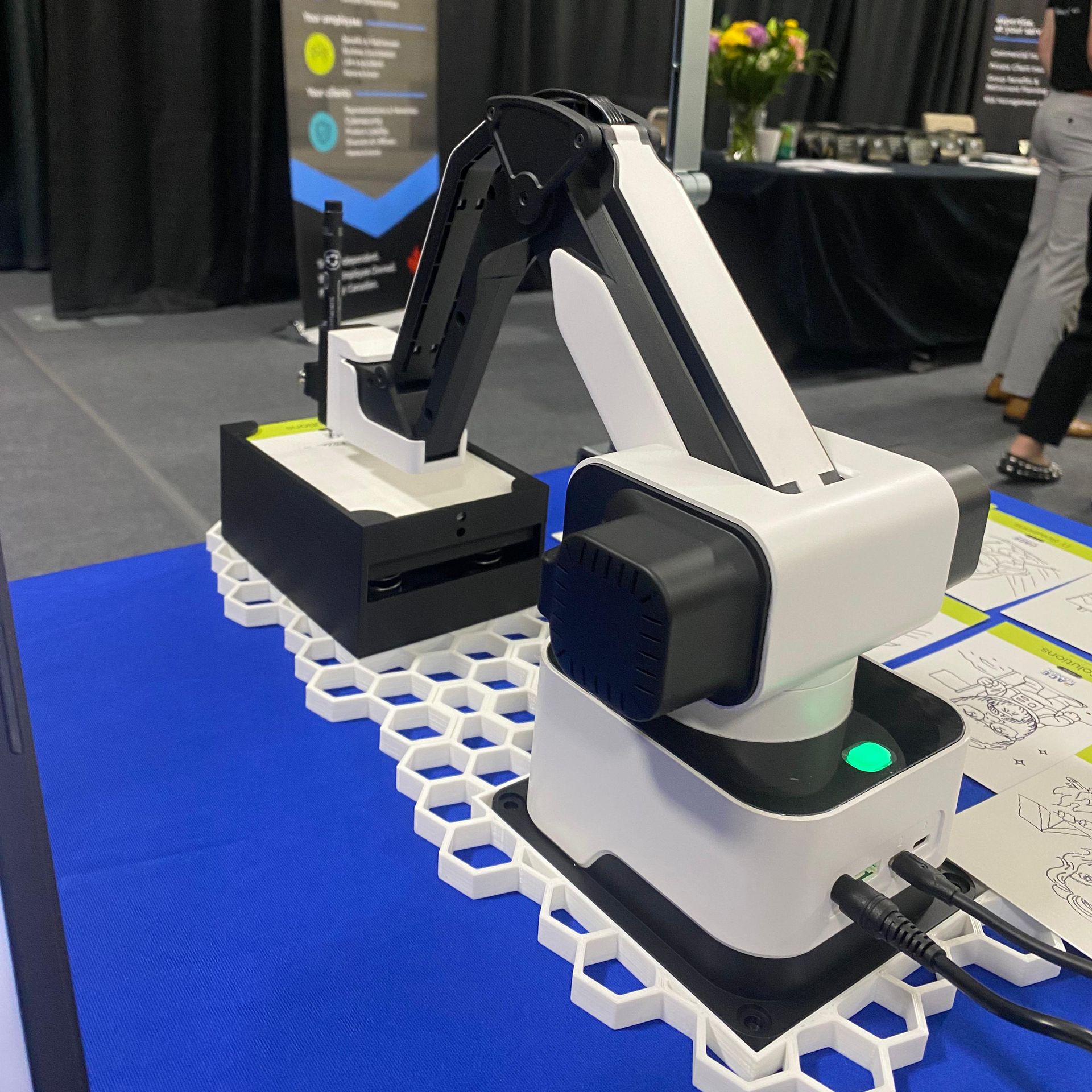 A robotic arm on a blue table at a conference; white and black with a green light.