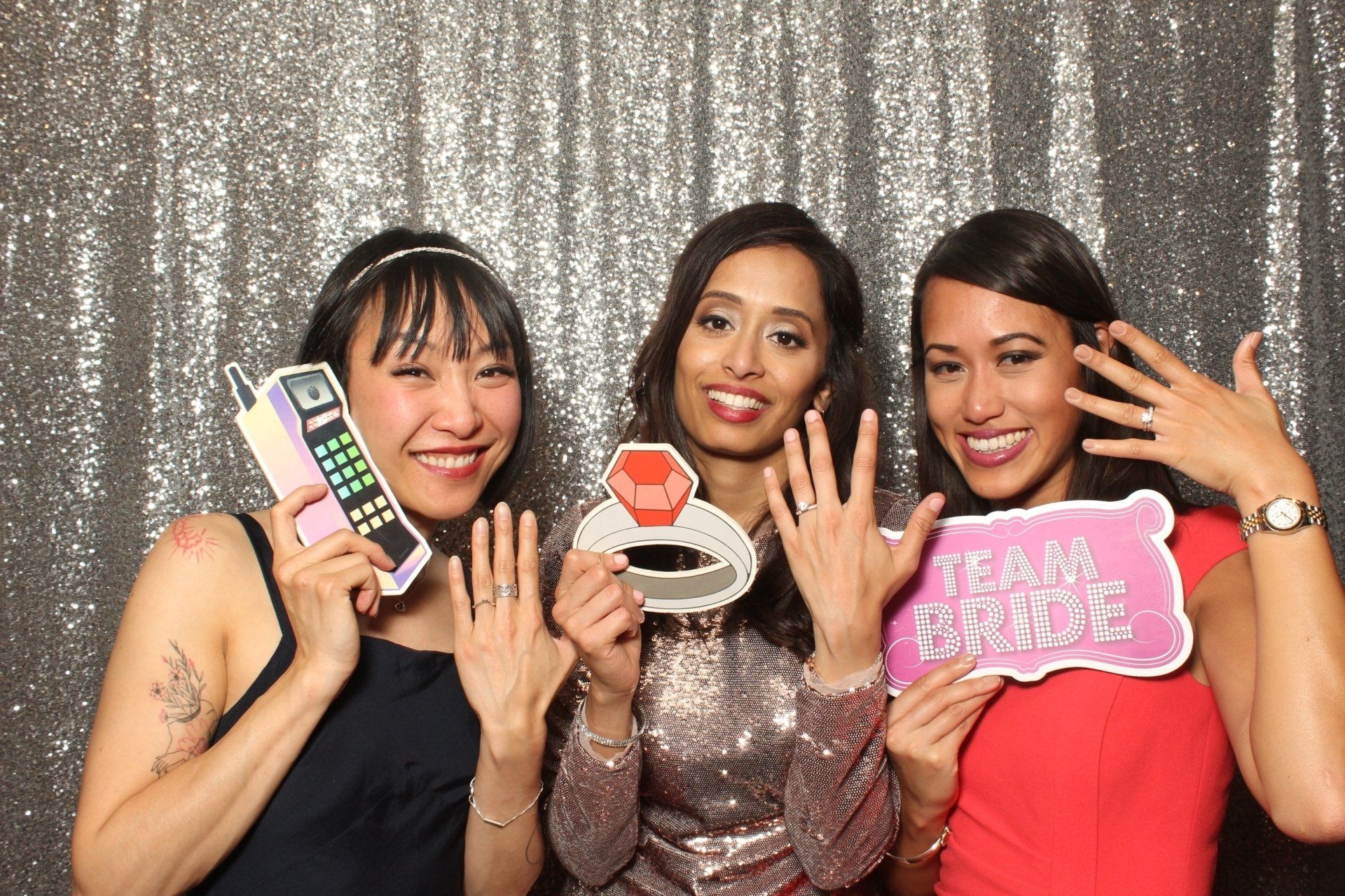 Three women at a party holding props: phone, ring, and
