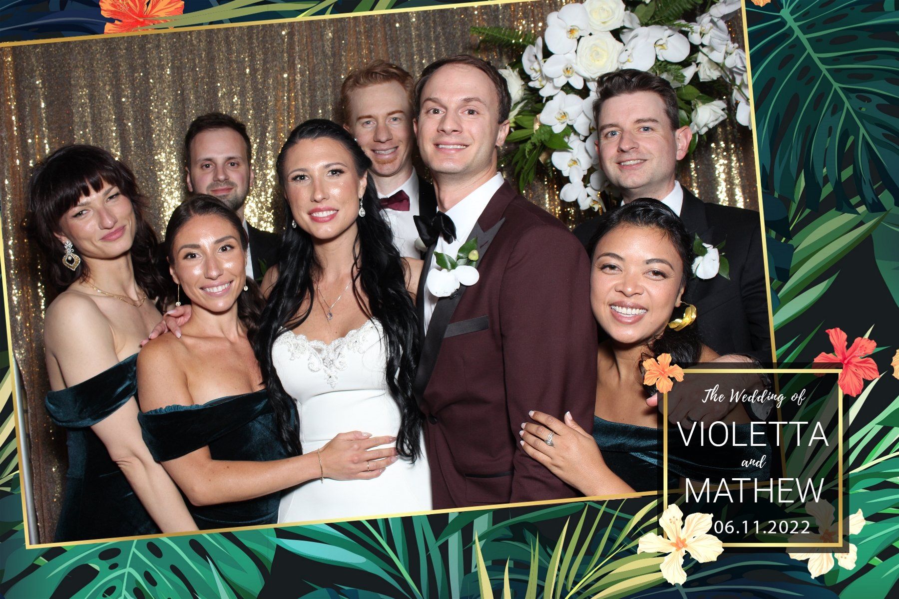 Wedding photo booth picture of a bride and groom with their wedding party, posing in front of a gold sequin backdrop.