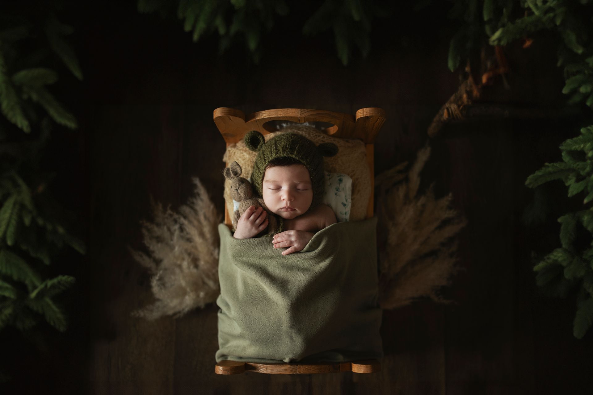 Un bambino dorme in un letto di legno, indossa un cappello verde a forma di orso ed è circondato dal verde e da tessuti morbidi.