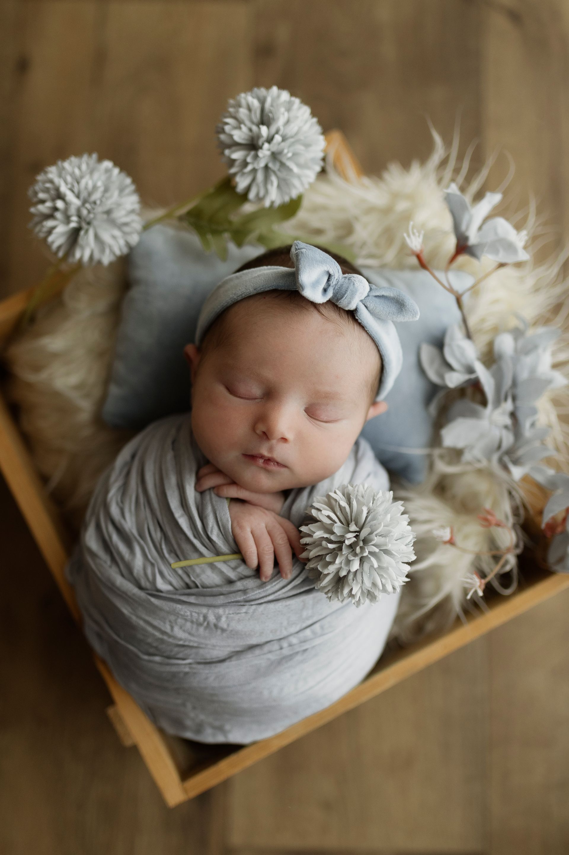 Neonato avvolto in un panno grigio, dorme tranquillamente in una scatola di legno con decorazioni soffici e una fascia per la testa.