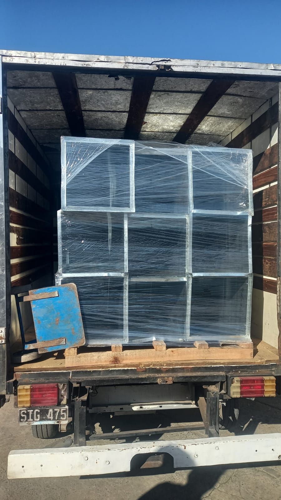 La caja de un camión estaba cargada con cajas y paletas apiladas y envueltas en plástico retráctil, bajo una lona blanca.