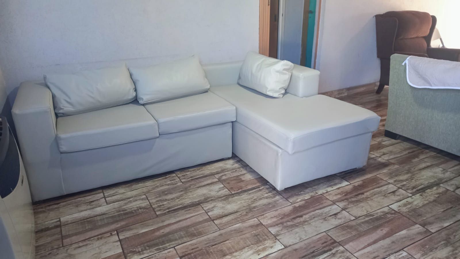 Sala de estar con sofá seccional gris claro, otomana y suelo con aspecto de madera.