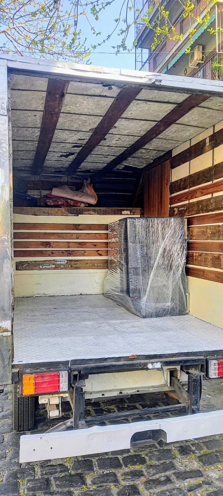Camión de carga con la parte trasera abierta, paneles de madera apilados y un gran paquete envuelto en su interior.