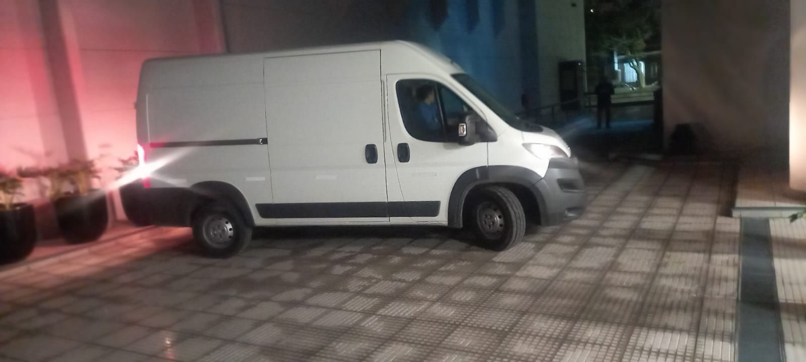 Furgoneta de carga blanca aparcada en una entrada de baldosas por la noche junto a un edificio con iluminación rosa.