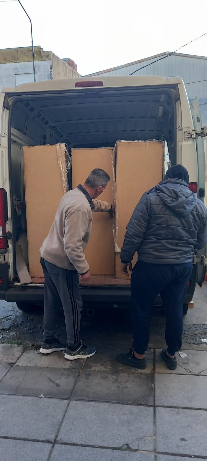 Dos personas descargando cajas de cartón de la parte trasera de un camión en una acera.