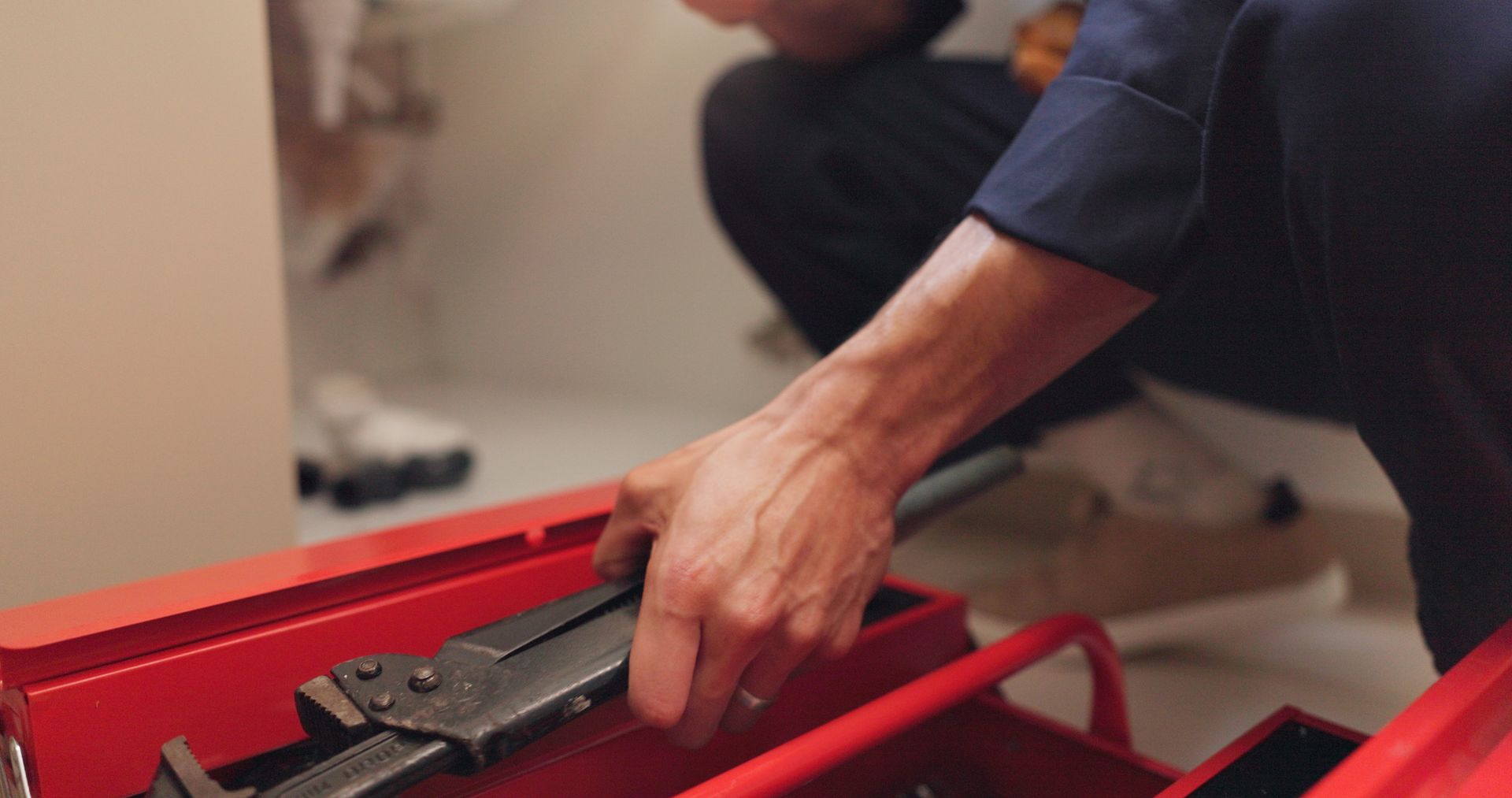 Hand reaching into a red toolbox to grab a metal tool Hand reaching into a red toolbox to grab a metal tool