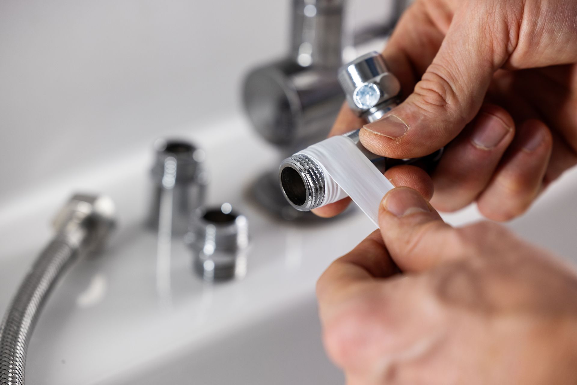 Hands wrapping white tape around a metal faucet pipe over a sink