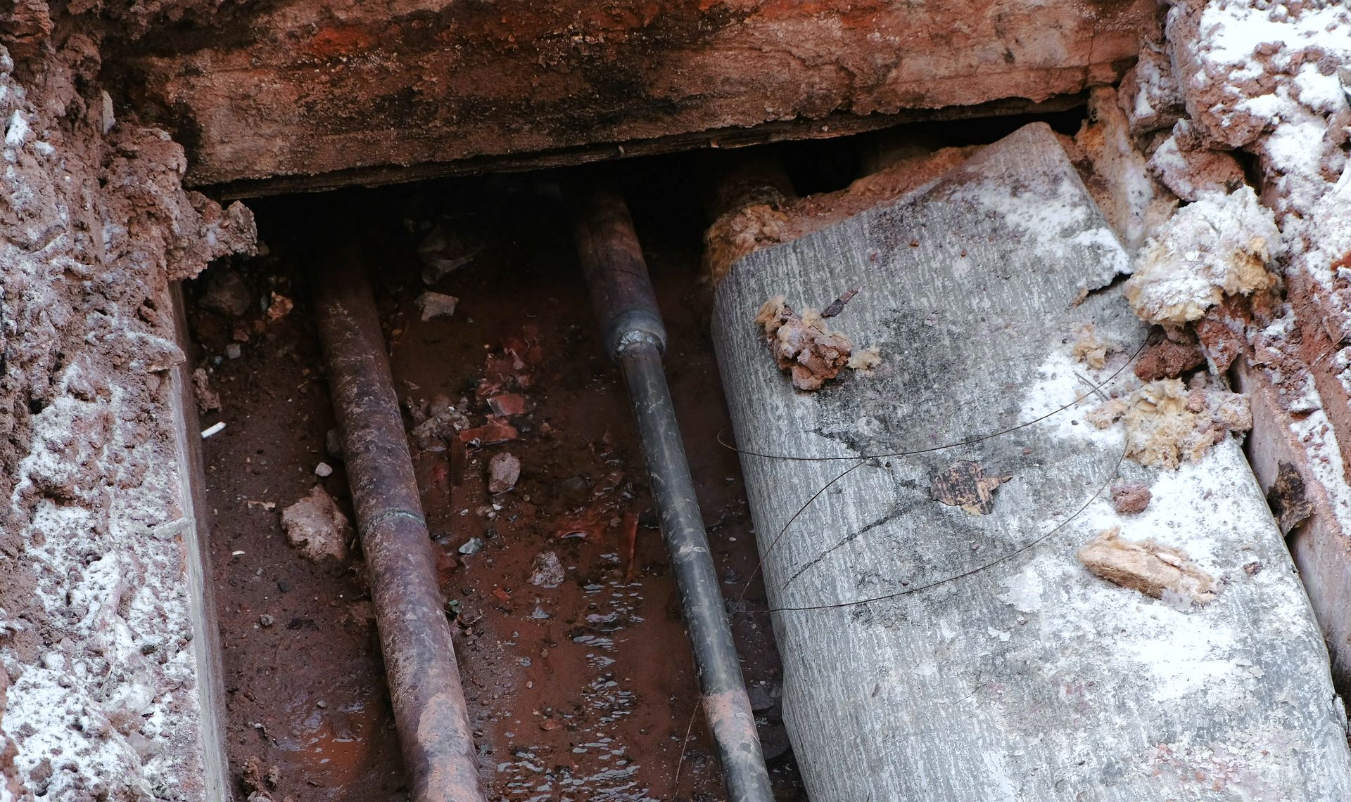 Rusted metal pipes under a rough concrete opening with dirt and debris around them