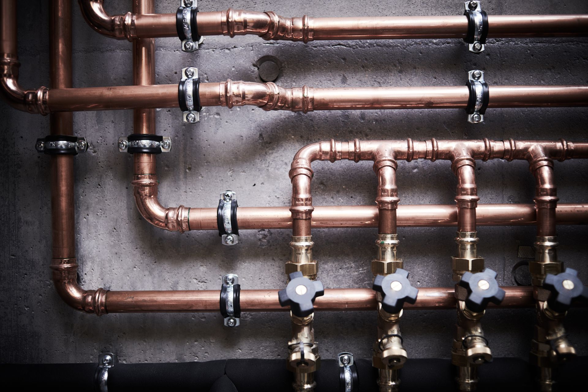 Copper water pipes and valves arranged horizontally on a wall in an industrial setting