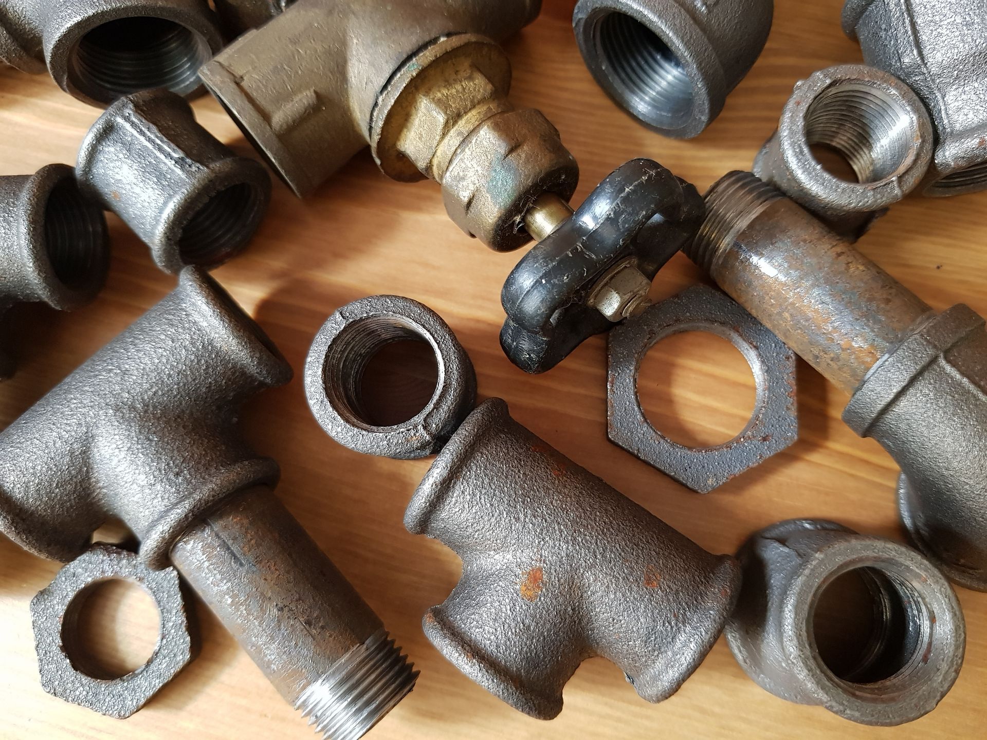 Assorted metal pipe fittings and connectors scattered on a wooden surface