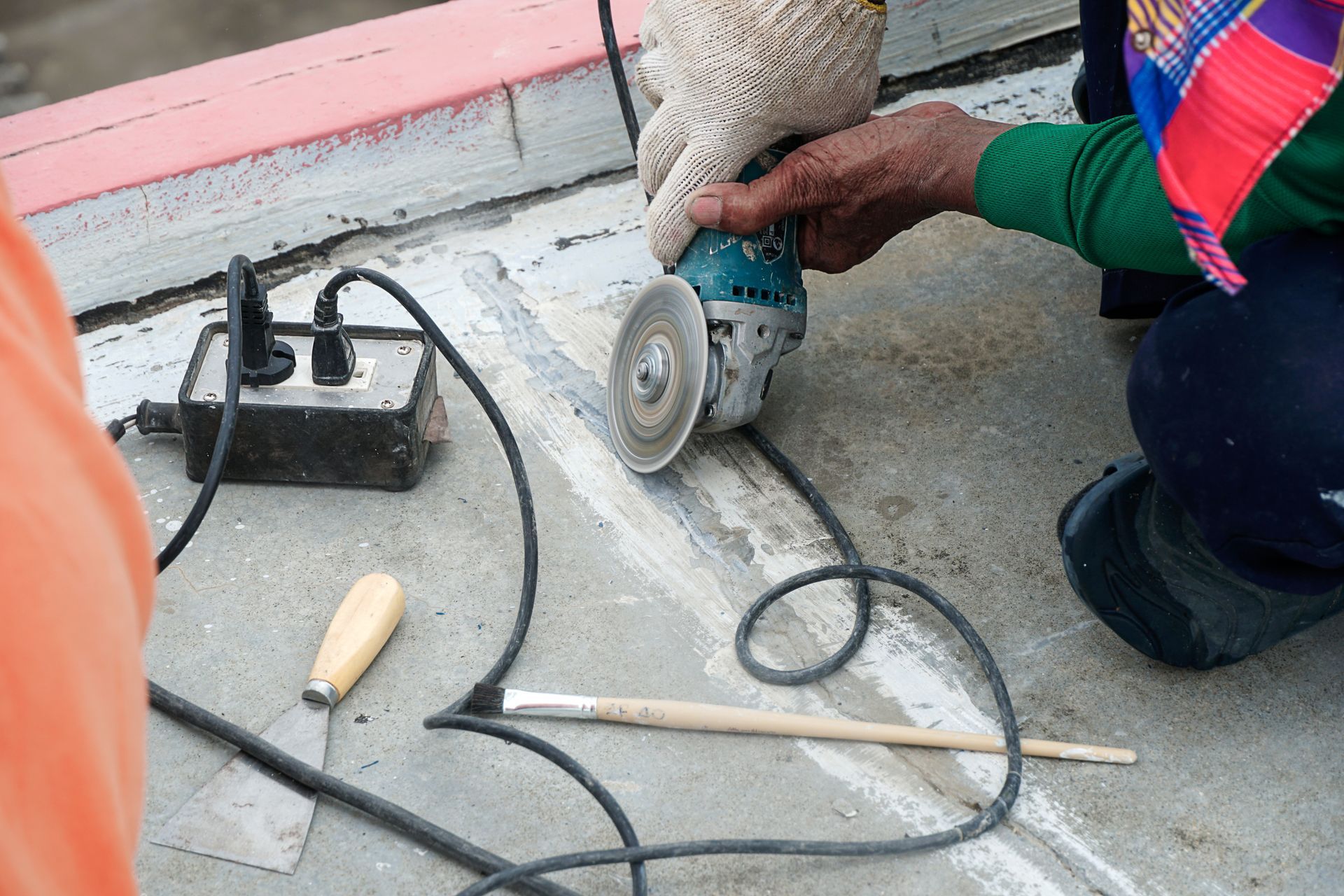 Worker using a power grinder on a concrete floor near tools and electrical cords.
