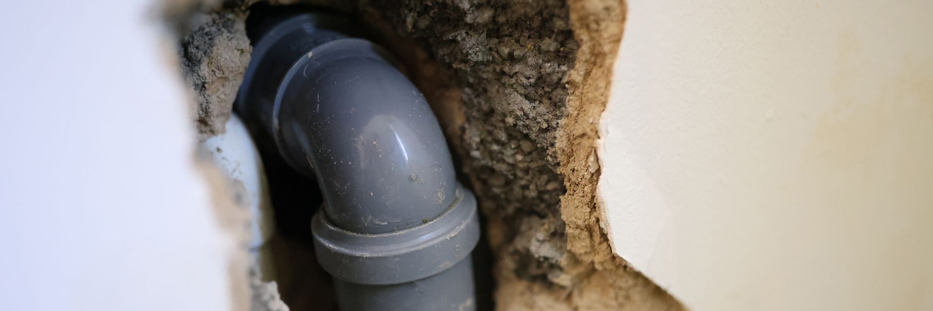 Gray PVC pipe elbow inside a wall opening with exposed insulation around it