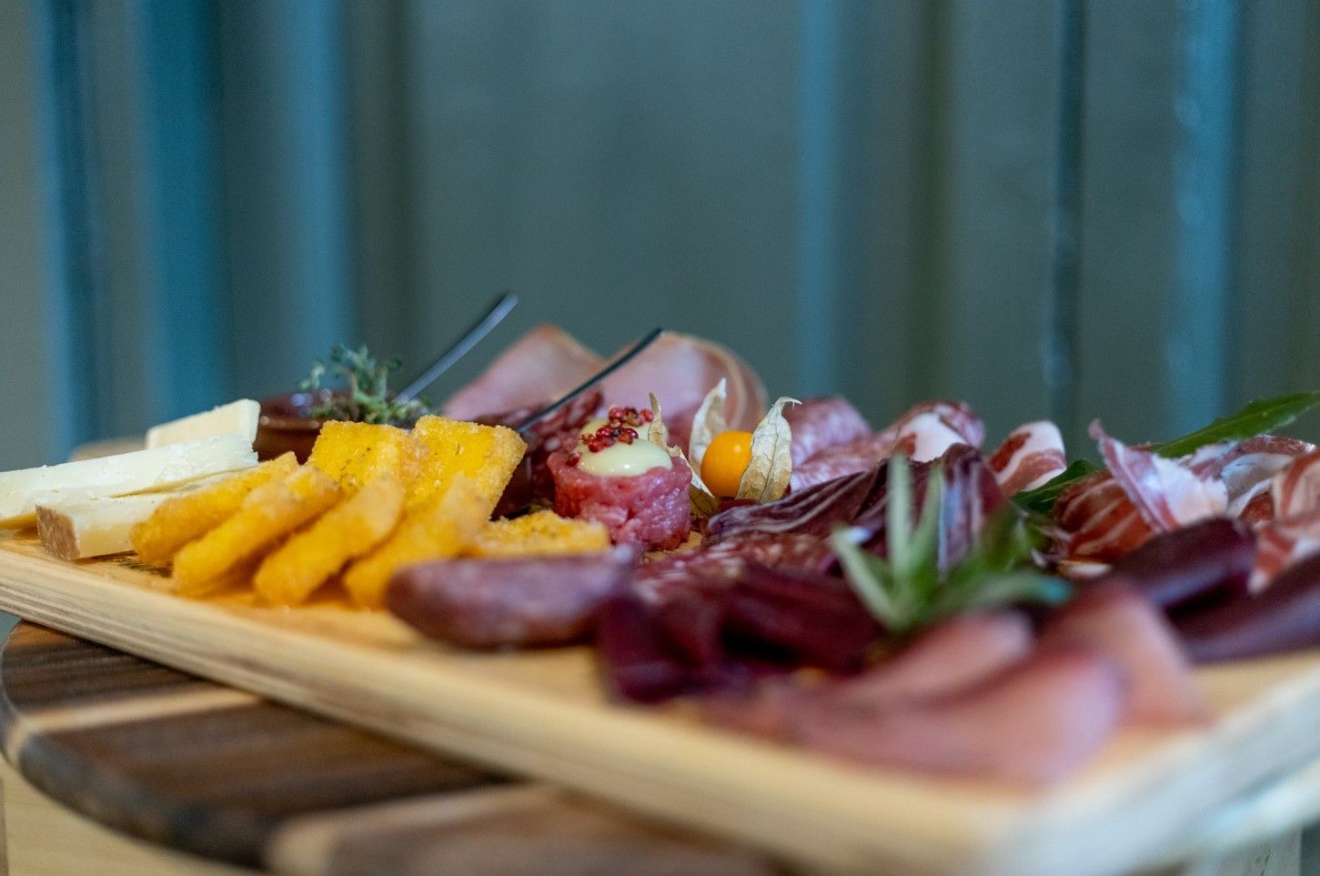 Un tagliere di legno con vari tipi di salumi, formaggi a fette e una piccola bacca dorata, adagiato su una superficie di legno.