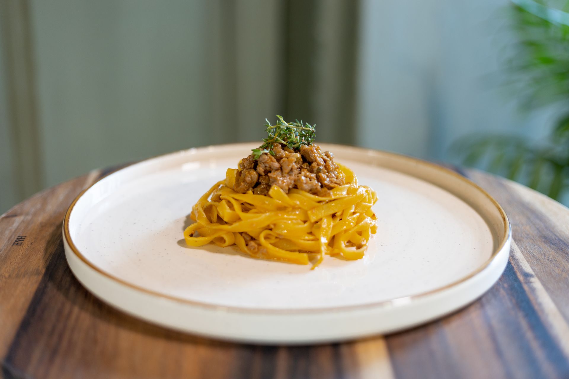 Un mucchio di fettuccine color giallo dorato, condite con saporita carne macinata ed erbe aromatiche fresche, adagiate su un piatto bianco.