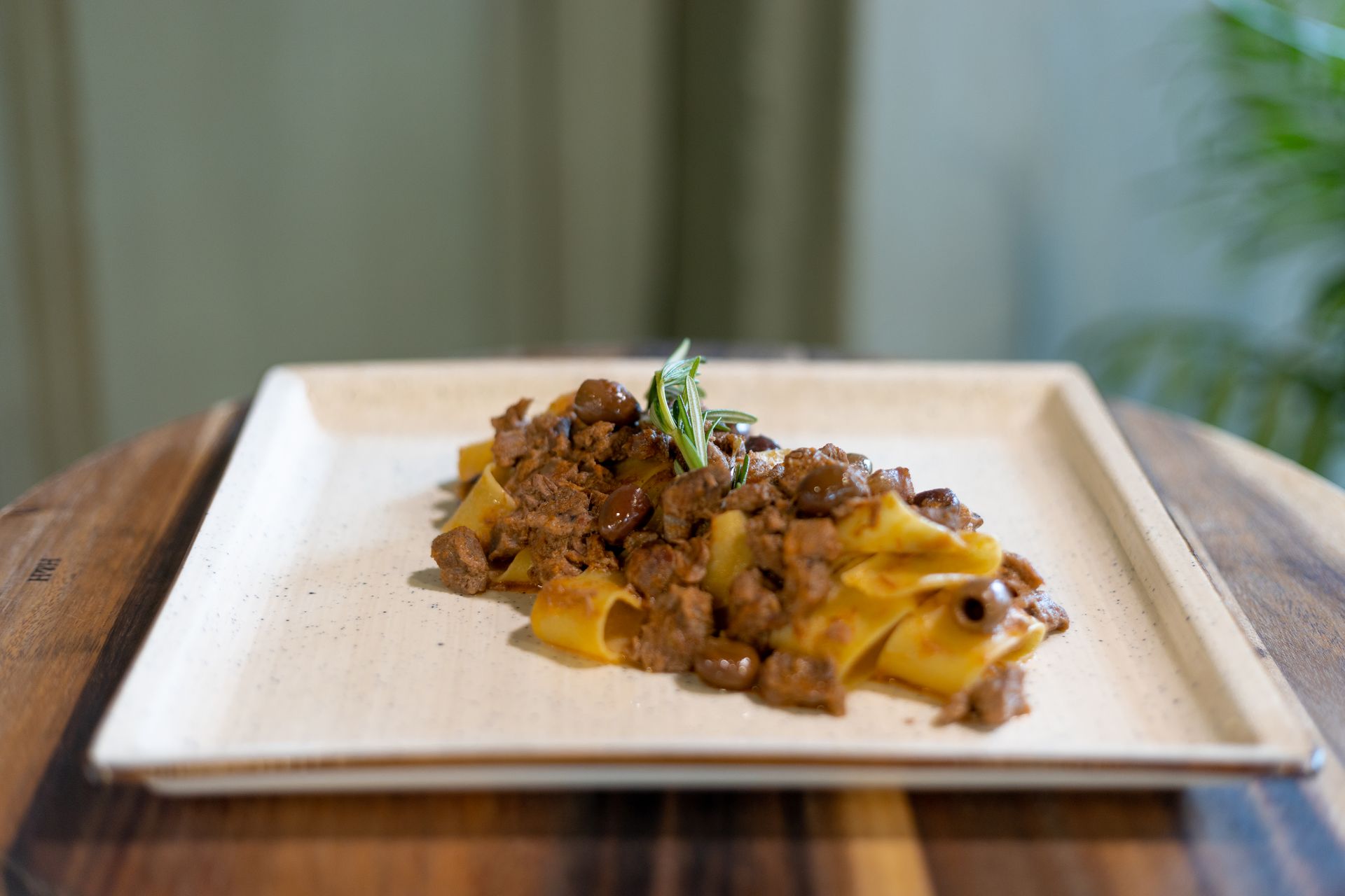 Un piatto di larghe pappardelle condite con un ricco ragù di carne e guarnite con erbe aromatiche fresche.