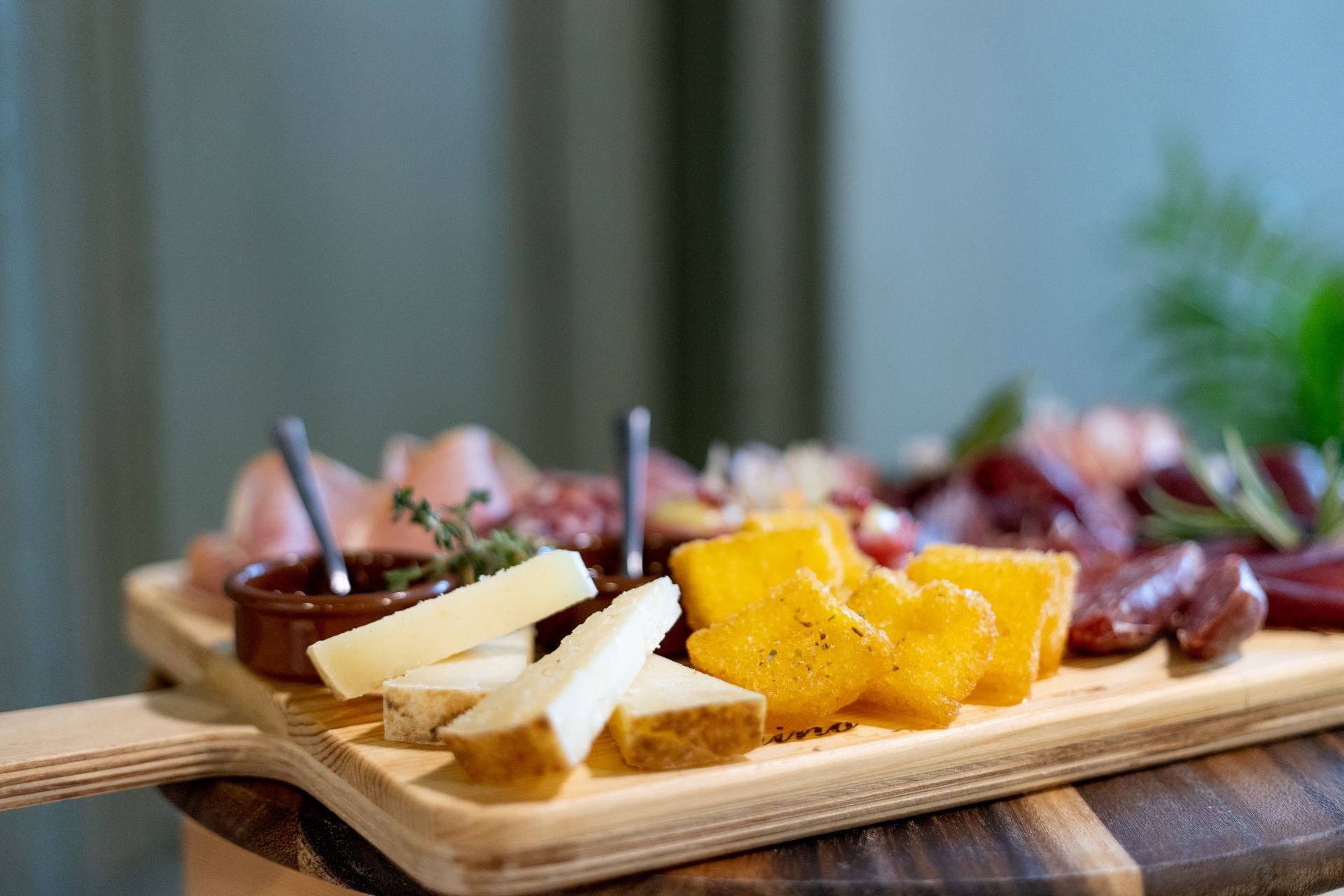 Un tagliere di legno con fette di formaggio, croccanti bocconcini di polenta, salumi e una piccola ciotolina di salsa.