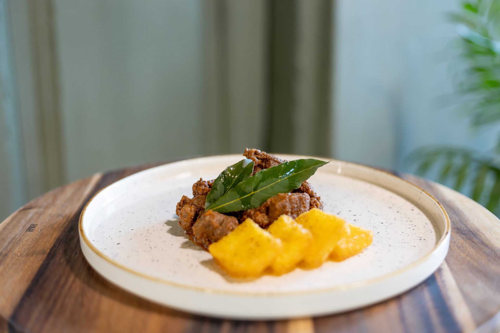 Un piatto con carne condita, guarnito con foglie verdi e accompagnato da fette di mango giallo, servito su un piano di legno.