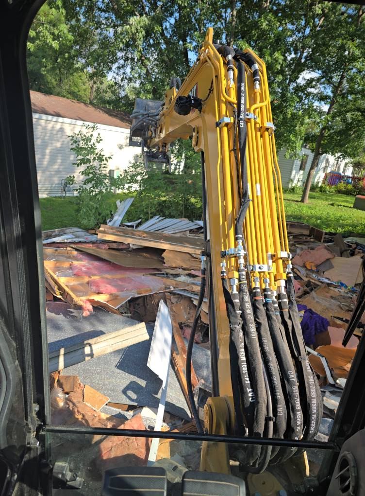 Yellow excavator demolishing debris in a residential driveway.