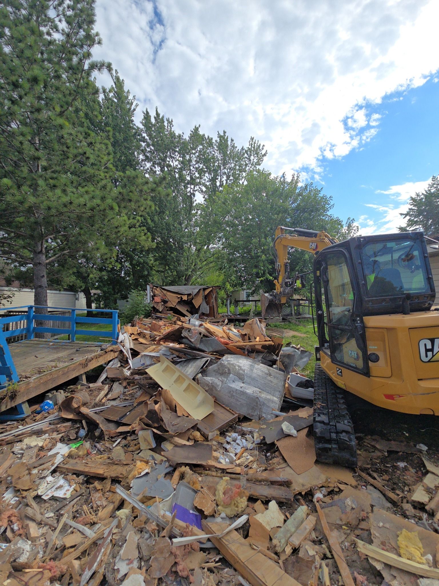 Demolition site: Yellow excavator tearing down a structure amidst debris under a cloudy sky.