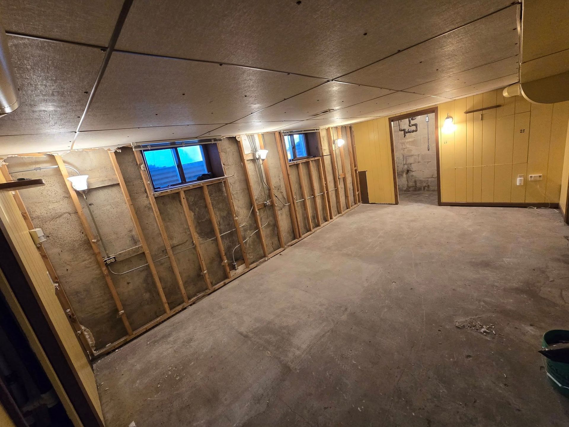 Basement interior renovation in progress, exposed studs on walls, concrete floor, small windows.