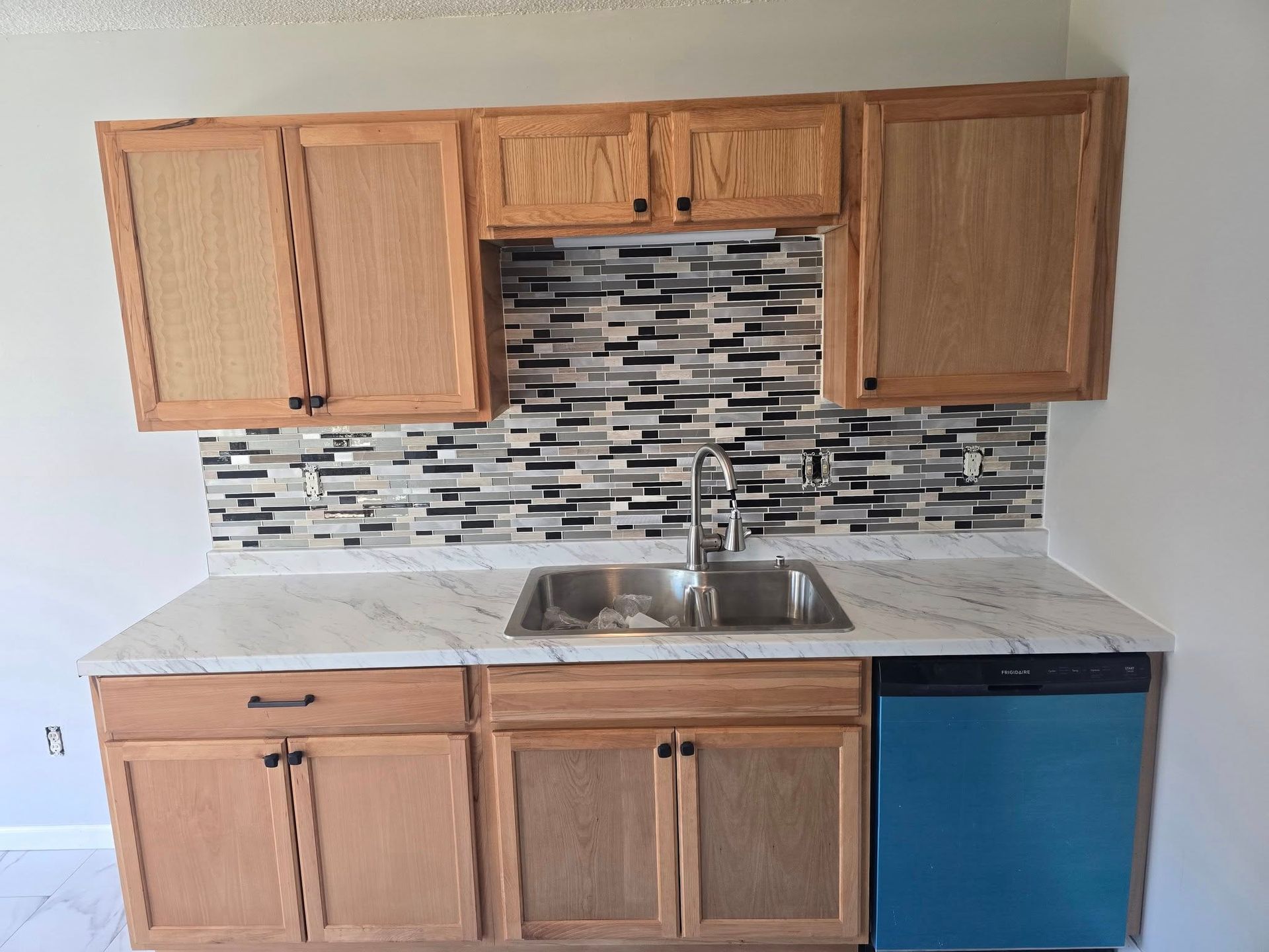 Kitchen with light wood cabinets, white countertops, stainless steel sink, and blue dishwasher.
