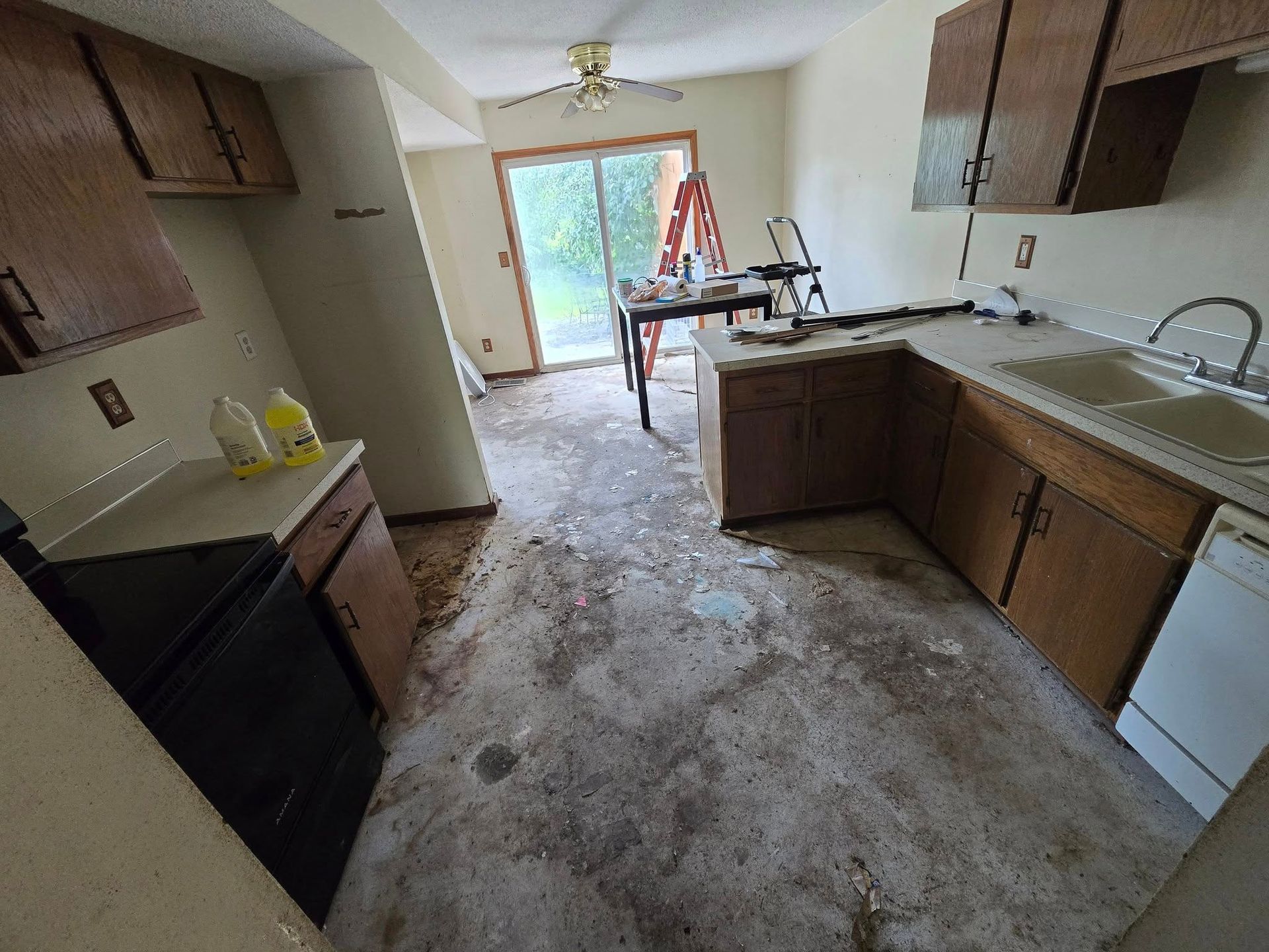 Kitchen with brown cabinets, debris on floor, and open sliding door.