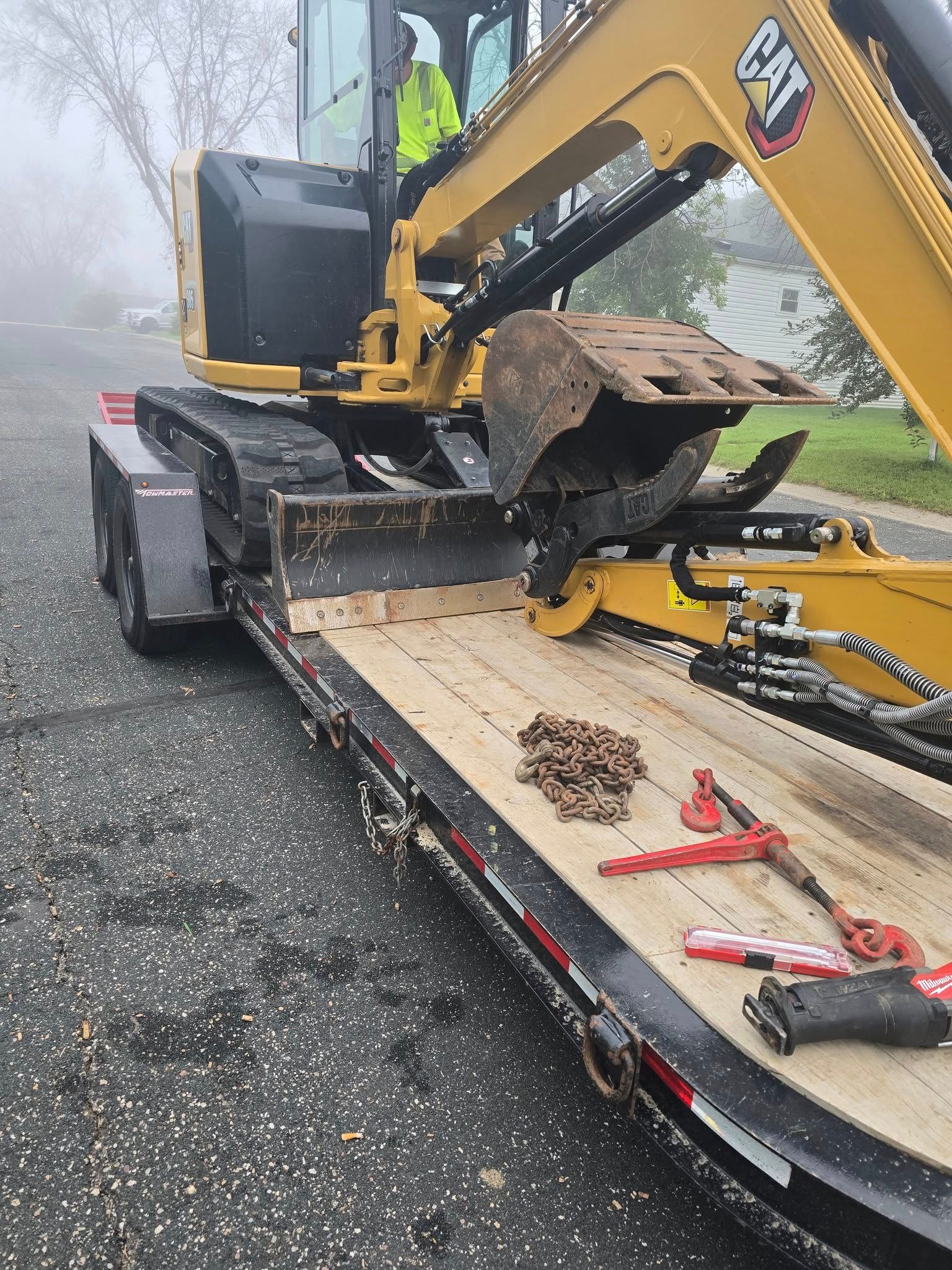 Yellow excavator on a trailer on a gray paved road, in a foggy setting.