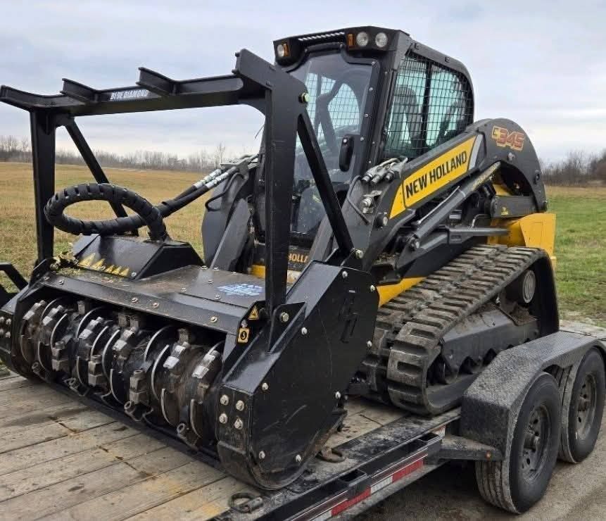 Yellow and black New Holland skid steer with a mulching head on a trailer in a field.