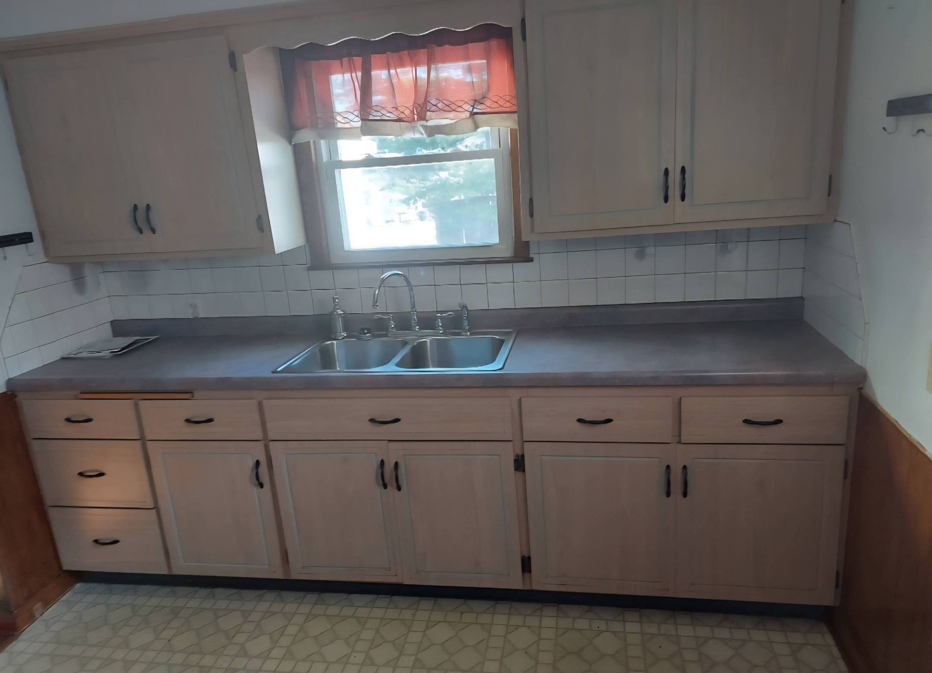 Kitchen with light-colored cabinets, sink, window, and countertop. Floor is tiled.