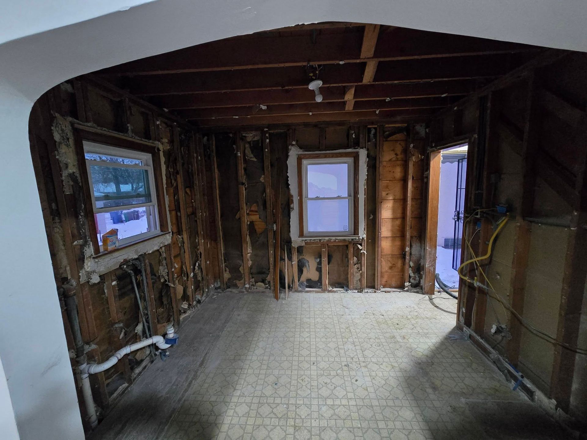 Room stripped to studs with two windows, doorway, and arched entryway.