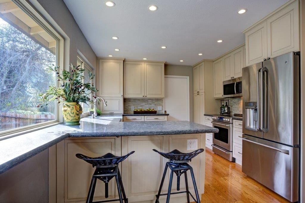 Bright modern kitchen with island, bar stools, large window, and stainless steel refrigerator and oven.
