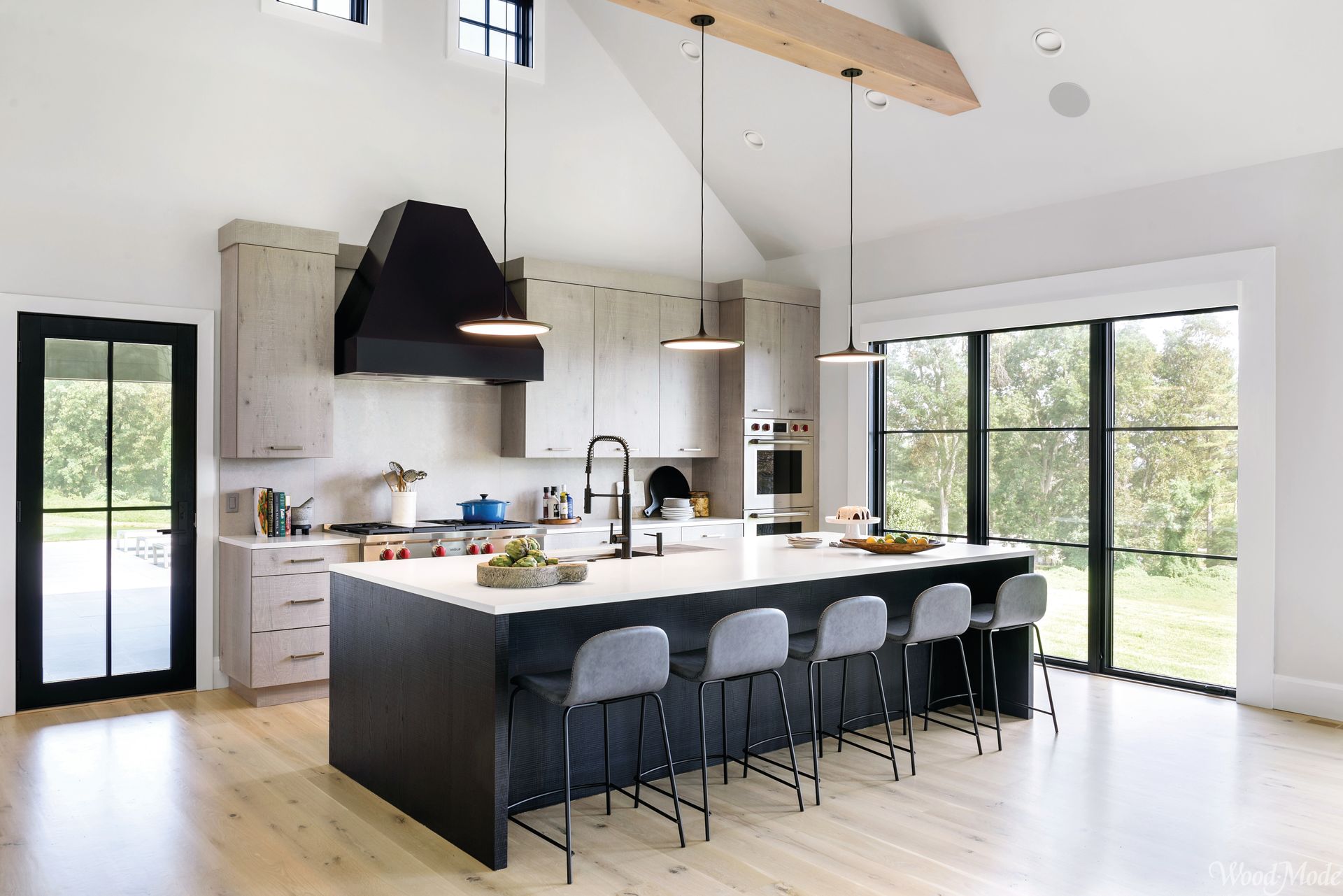 Modern open kitchen with large island, white cabinets, black range hood, and floor-to-ceiling windows