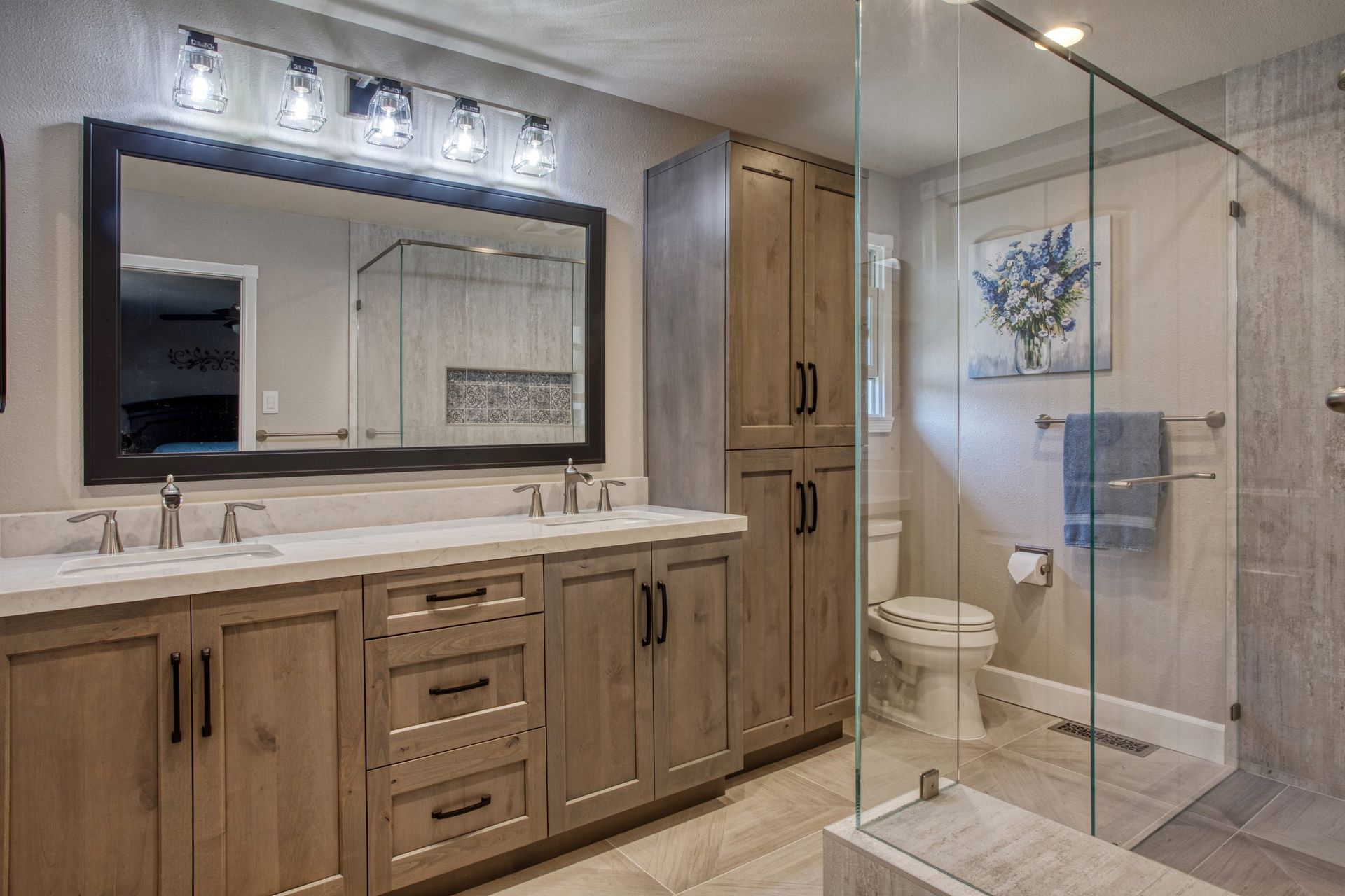 Modern bathroom with wood vanity, large mirror, and glass-enclosed shower with toilet.