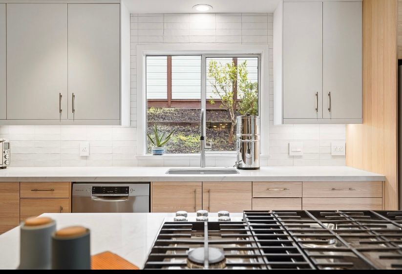 Bright modern kitchen with white cabinets, wood accents, and a window above the sink