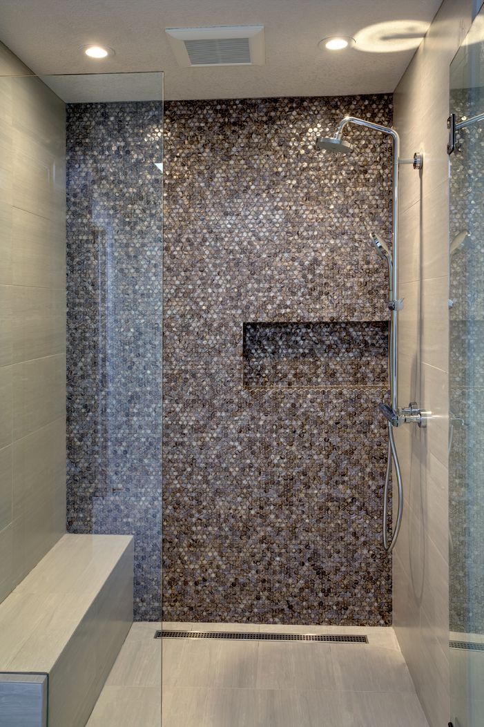 Modern shower stall with dark mosaic tile wall, glass door, and white tub edge