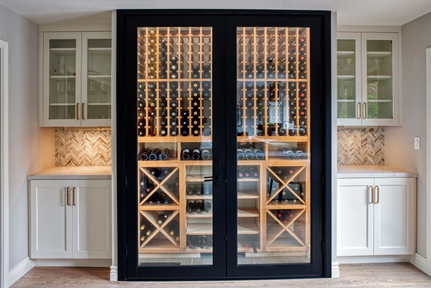 Built-in wine cabinet with glass doors and illuminated racks between white kitchen cabinets