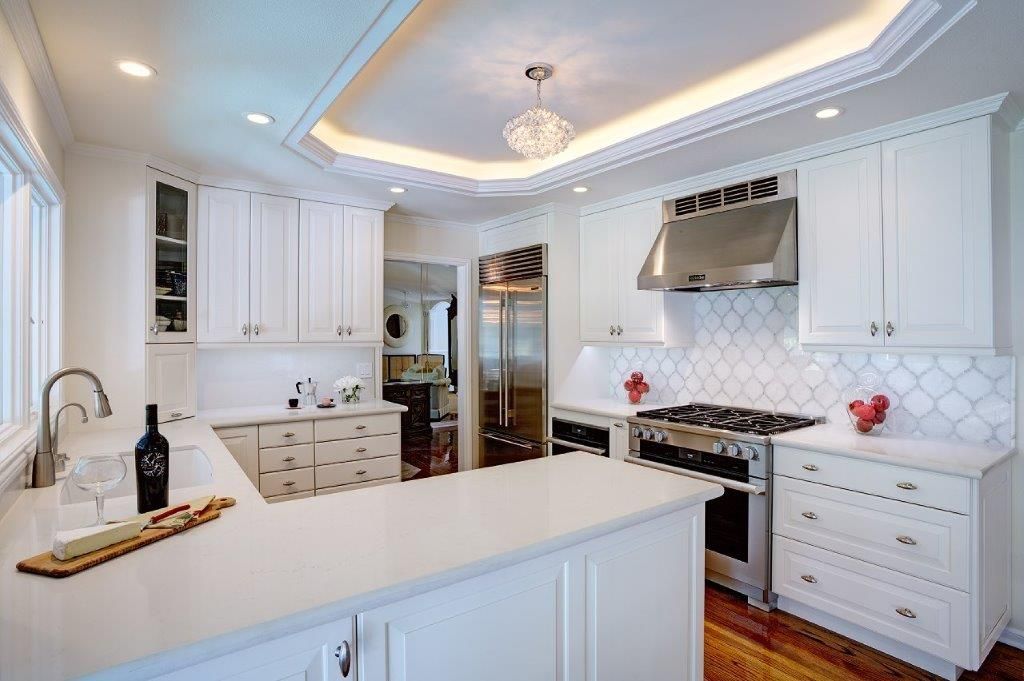 Bright white modern kitchen with large island, stainless stove, and tray ceiling with chandelier.