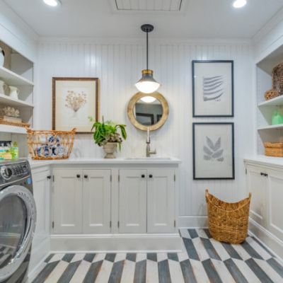 Bright laundry room with white cabinets, round mirror, hanging light, woven baskets, and striped floor tiles