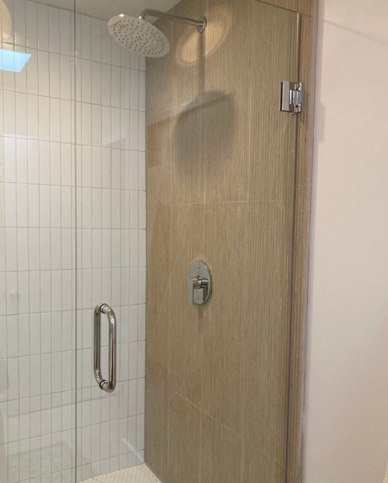 Shower stall with glass door, chrome handle, and wall-mounted showerhead in a tiled bathroom