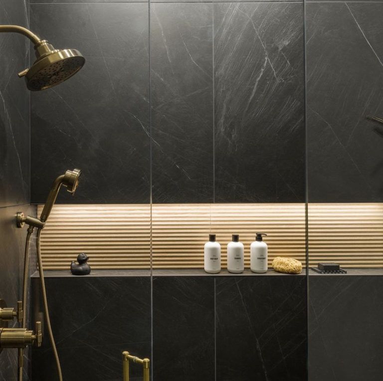 Modern dark-tiled shower with brass fixtures and toiletries on a shelf
