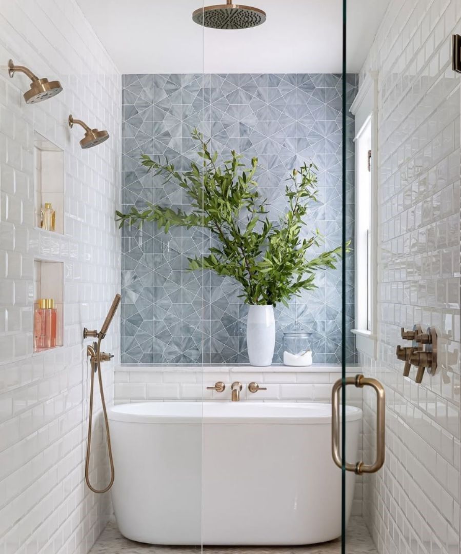 Modern white bathroom with a freestanding tub, gold fixtures, tiled walls, and a vase of greenery