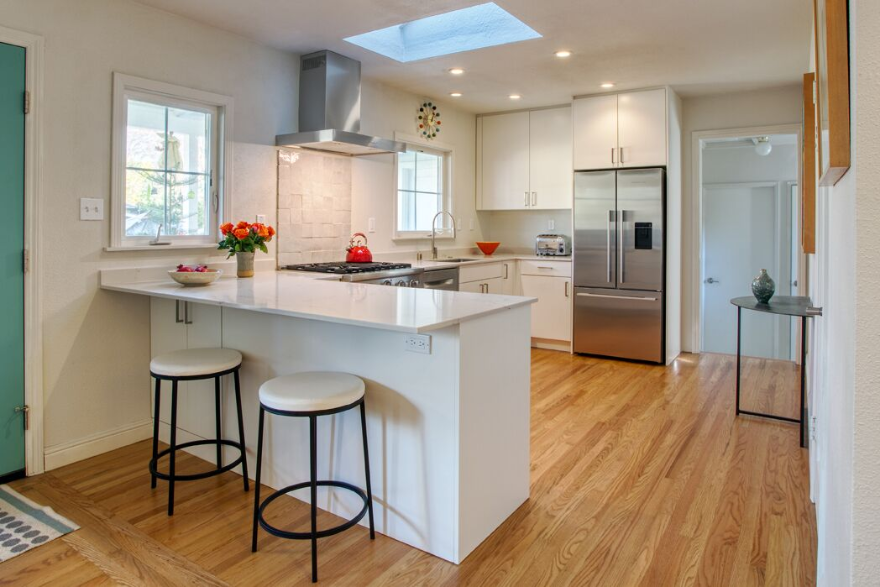 Bright modern kitchen with white cabinets, island stools, stainless steel appliances, and wood flooring