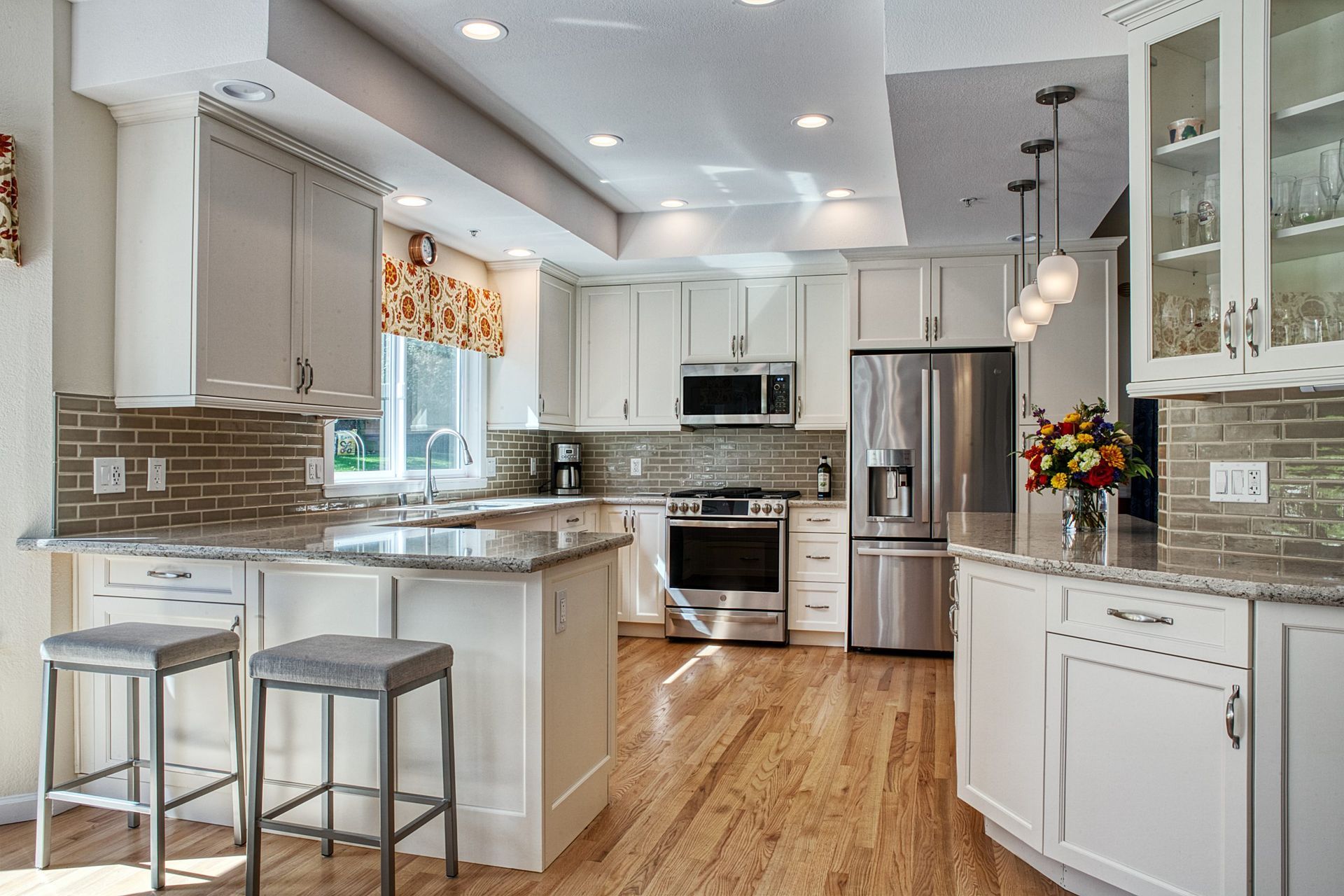 Bright modern kitchen with white cabinets, stainless appliances, island seating, and hardwood floors